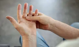 Person massiert Hand, da die Finger schmerzen beim Beugen.
