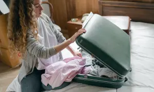 Kobieta pakuje różowe koszule do zielonej walizki, przygotowując się do podróży.