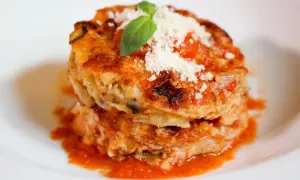 Parmigiana di alici, un tortino stratificato con pesce, verdure e pomodoro, guarnito con basilico e parmigiano.
