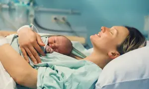 Szczęśliwa mama tuli noworodka. To drugie dziecko, na które przysługuje 1000 zł.