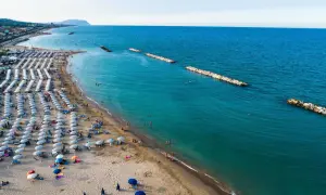 Ampia spiaggia libera a Civitanova Marche, con file ordinate di ombrelloni e lettini, bagnanti che si godono il mare turchese e dighe frangiflutti in pietra.