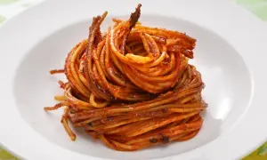 Spaghetti all'assassina, lekko przypieczone, w intensywnym sosie pomidorowym, ułożone na białym talerzu.