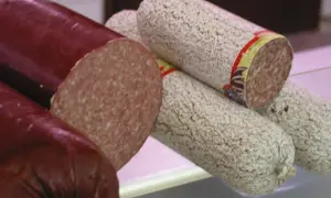 Kawałki ciemnej i jasnej kiełbasy salami, jedna przekrojona.