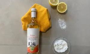 Bottiglia di aceto di vino bianco, limoni, panno giallo e bicarbonato: ingredienti naturali per uno sgrassatore fatto in casa.