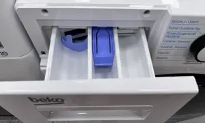Szuflada pralki Beko z przegródkami. W środkowej, fioletowej przegródce, gdzie wlać płyn do płukania, znajduje się symbol kwiatka.
