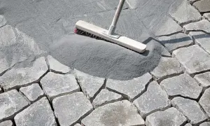 Besen verteilt feinen Fugensand auf Pflastersteinen. Der Sand dient als effektiver Fugensand gegen Unkraut und stabilisiert die Steine.