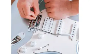 Ręce montują nową strunę do mostka gitary elektrycznej. Praktyczny poradnik, jak zmienić struny w gitarze elektrycznej.