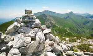 Cairn con M. 2102, simbolo di un'avventura di trekking nei Monti Sibillini. Panoramica mozzafiato sulle verdi valli e sentieri tortuosi.
