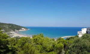 Vista panoramica della baia dei trabucchi con mare azzurro, spiaggia affollata e vegetazione rigogliosa.