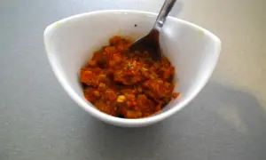 W białej miseczce znajduje się aromatyczna, czerwona pasta curry, gotowa do dodania smaku potrawom. Łyżeczka czeka, by nabrać jej porcję.