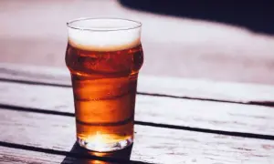 Un bicchiere di caña birra con schiuma bianca, illuminato dal sole, su un tavolo di legno all'aperto.