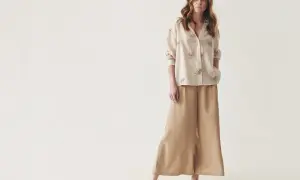 Kobieta w beżowych kulotach i bluzce z haftem. Idealne buty do kulotów to wygodne sandały, jak te na zdjęciu.