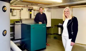Ein Mann und eine Frau stehen neben einem grünen Nano BHKW-Gerät in einem Heizungsraum.