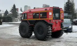 Czerwone auto straż pożarna z wielkimi oponami, gotowe do akcji w trudnym terenie.