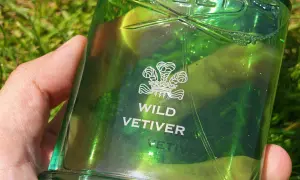 Zielona butelka perfum Creed Wild Vetiver w dłoni na tle trawy.