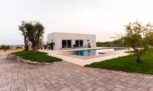 Pavimentazione esterna texture con blocchi di pietra color ruggine e beige, che circonda una piscina moderna e un prato verde.