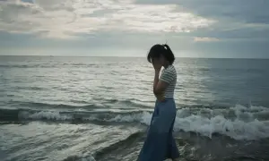 Kobieta na plaży, zakrywająca twarz dłońmi, symbolizuje objawy depresji.