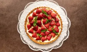 Ein köstlicher Erdbeerkuchen mit Pudding, garniert mit frischen Erdbeeren und Minze, auf einer zarten Papierspitze.