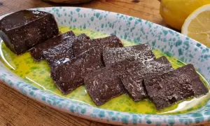 Fette di salame di tonno scuro, lucido e saporito, servite in una ciotola con olio verde e limone.