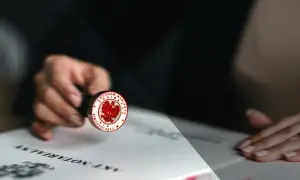 Dłoń trzyma pieczęć notarialną z orłem, gotową do złożenia podpisu na akcie poświadczenia dziedziczenia.