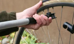 Dłoń trzyma pompkę przy wentylu, sprawdzając jakie ciśnienie w rowerze jest optymalne.