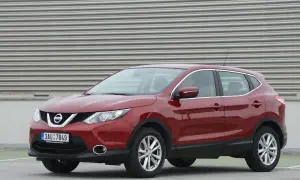 Czerwony Nissan Qashqai J11, z widocznym wykazem żarówek w przednich reflektorach, zaparkowany na tle falistej ściany.