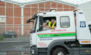 Un dépanneur en uniforme jaune regarde par la fenêtre d'un camion de dépannage. Le camion est marqué "ROLLIN DEPANNNAGE".
