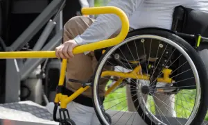 Persona in sedia a rotelle si aggrappa a un corrimano giallo, suggerendo un noleggio auto con legge 104 per maggiore accessibilità.