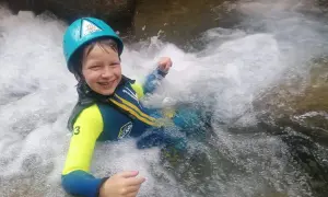 Niño sonriente con casco y traje de neopreno disfrutando del barranquismo en la Sierra de Guara. ¡Una aventura de senderismo acuático inolvidable!