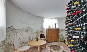 En vinkällare med en imponerande samling flaskor, perfekt för att lagra vin hemma. Ett runt bord med stolar och en gammal skåp ger rummet karaktär.