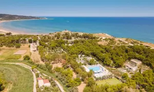 Vista aerea della baia della Tufara con mare azzurro, spiaggia dorata, pineta lussureggiante, piscina e campo da tennis.
