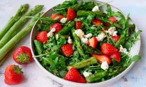 Frischer Spargelsalat mit Erdbeeren und Rucola, garniert mit zerbröseltem Käse.