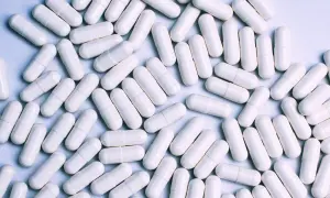 Mnóstwo białych kapsułek, niektóre z nich zawierają iwermektynę, leżą luźno na jasnym tle.