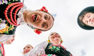 Uśmiechnięci młodzi ludzie w barwnych strojach ludowych, celebrujący polski folklor.
