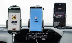 Trzy telefony w uchwytach na desce rozdzielczej: z lewej Rysiek, w środku Waze, a po prawej Yanosik. Którą nawigację wybierzesz?