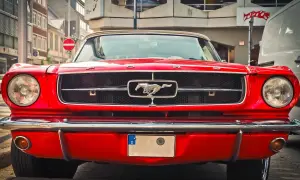 Klasyczny, czerwony Ford Mustang, jeden z kultowych amerykańskich samochodów, z błyszczącym chromowanym grillem i koniem w galopie.