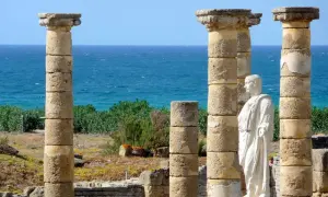 Ruinas romanas en la playa Baelo Claudia, con columnas y una estatua de mármol frente al mar azul.