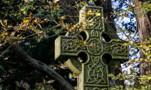 Kamienny krzyż celtycki z misternymi wzorami, otoczony jesiennymi liśćmi. Symbolizuje wieczność i połączenie życia.