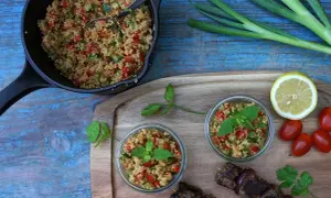 Frischer Couscous-Salat mit Tomaten, Gurken und Minze, serviert in Gläsern und einer Pfanne, daneben ein Spieß mit Fleisch.