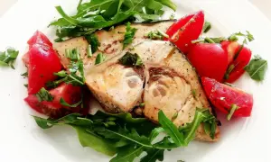 Spiedini di pesce spada in padella con pomodorini freschi e rucola, un piatto leggero e saporito.