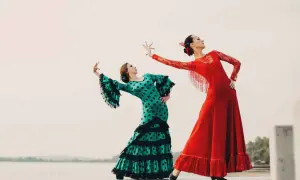 Dos mujeres bailan flamenco. Una con vestido verde de lunares, la otra con rojo. Inspiración para palos del flamenco para niños.