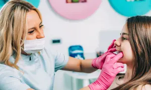 Ortodonta w różowych rękawiczkach zakłada aparat na zęby młodej pacjentce.