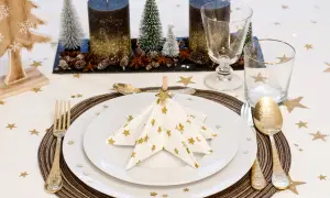 Vacker nyårsdukning med vita servetter med guldig stjärndekor, som en julgran. Guldiga bestick och stjärnformad duk.