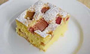 Puszyste ciasto z rabarbarem, posypane cukrem pudrem, na białym talerzu. Idealne na letnie popołudnie.