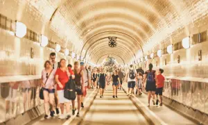 Menschen gehen durch den hell erleuchteten, gewölbten Gang des alten Elbtunnels.