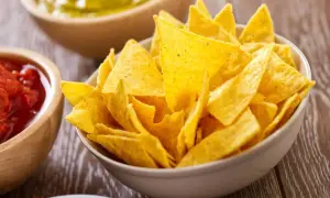 Nachos amarillos en un tazón, con salsa y guacamole al fondo.