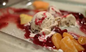 Cremiges Mascarpone Eis mit roter Fruchtsauce und Mandarinenstücken auf einem Teller.