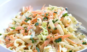 Chinakohl-Salat mit Karottenstreifen und Petersilie in einer weißen Schüssel.