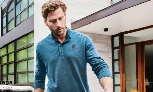 Mann trägt ein blaues Henley Shirt mit Knopfleiste und rotem Logo. Was ist ein Henley Shirt? Ein lässiges Oberteil mit Kragen und Knopfleiste.