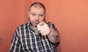 Mężczyzna w kratę wskazuje palcem, na ramieniu tatuaż z Indianinem. "234 kk" - czy to jego numer?